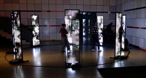 8 LED screens in a circle displaying black and white abstract content and with people